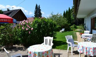 A beautiful garden with colorful tables and chairs. In the background, green plants and a clear blue sky can be seen.