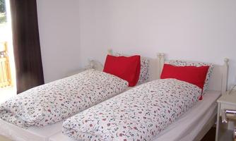 A cozy bedroom with two single beds. The bedding is decorated with a floral pattern in gentle colors and red cushions.