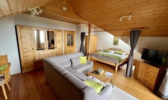 A cozy room with a wooden ceiling and furniture. There is a bed, a seating area, and a television.