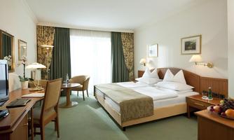 A modern hotel room with two beds, a table and chairs. Large windows provide plenty of daylight.