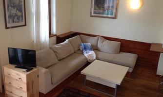 A cozy living room with a comfortable couch and a coffee table. Pictures hang on the wall and there is a small television on a wooden cabinet.