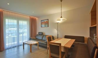 A modern living room with a cozy sofa, a dining area, and a large window. The room atmosphere is bright and inviting.