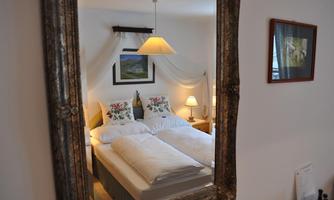 A cozy bedroom with two beds and decorative cushions. In the background, there is a lamp and a framed picture.