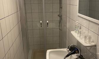 A modern bathroom with a shower and a sink. The walls are tiled, and hanging towels are available.