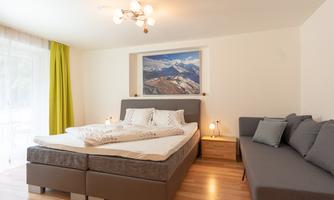 A modern bedroom with a large bed and a cozy couch. Bright and cheerful with a window that looks out on the mountains.