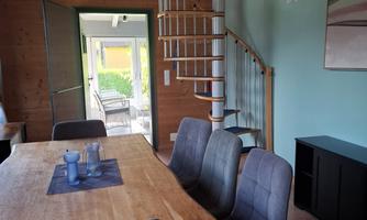 A cozy dining area with a wooden table and modern chairs. A spiral staircase leads to an upper area in a bright, stylish room.