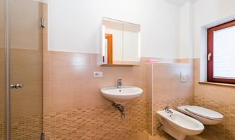 A modern bathroom with a shower, sink, and bidet. The walls are in neutral colors and there is a window with a view outside.