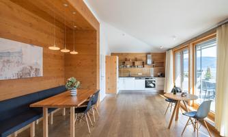 A modern-designed living space with wooden paneling and large windows. The area includes a dining space and a kitchen with modern appliances.