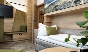 A modern hotel room with wooden paneling and a comfortable bed. A large landscape painting hangs on the wall, and a TV is visible.