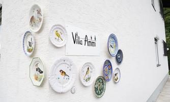 A white wall with a sign "Villa Amici" and colorful plates depicting various birds. The decoration gives the place a charming and inviting character.