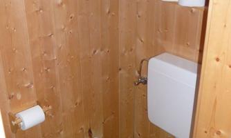 A small bathroom with wood paneling. It includes a toilet, a sink, and toilet paper.