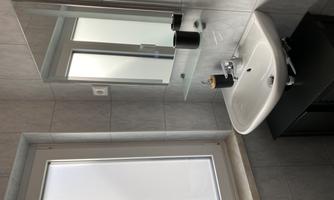 A modern bathroom with an elegant sink and a mirror. The window lets in a lot of daylight and the walls are tiled in light colors.