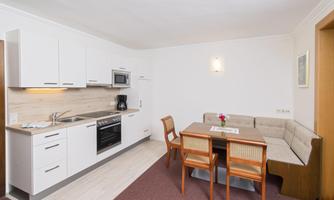 A modern kitchen with white cabinets and modern appliances. In the dining area, there is a table with chairs and a cozy seating area.