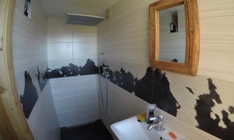 A modern bathroom with a shower and a sink. The walls are partially painted black, and there is a wooden mirror.