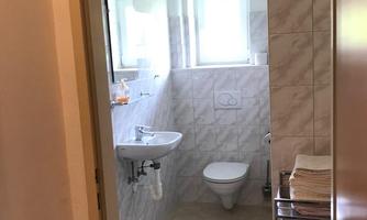 A clean bathroom with a toilet, a hand basin, and a window. Clean towels are neatly stacked.