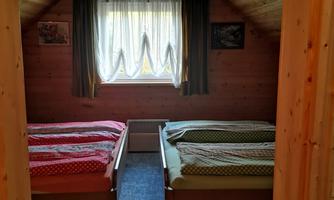 A cozy bedroom with two beds and wooden walls. The window provides plenty of daylight and an inviting atmosphere.