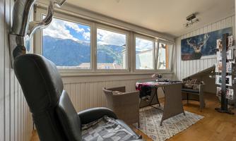 A cozy living space with a view of the mountains. The room is modernly furnished and has large windows that let in plenty of light.