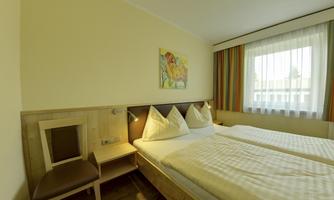 A bright hotel room with two beds, a chair, and a color picture on the wall. Large windows provide plenty of natural light.