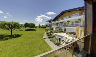 A modern accommodation with cozy balconies and a view of a green meadow. The surroundings are bright and inviting under a clear sky.