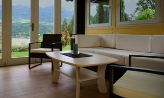 A cozy living area with a white sofa and a low table. The large windows offer a view of the mountains and nature.