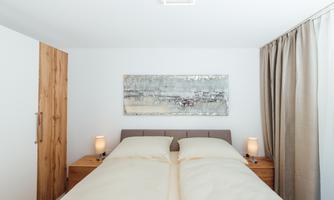 A modern bedroom with a double bed and two bedside lamps. The walls are painted light, and a painted picture hangs above the bed.