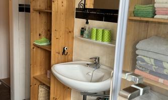 A modern bathroom with a sink and a mirror. On the walls, there are shelves with colorful towels and decorative baskets.