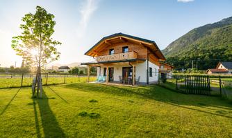 A beautiful wooden house with a large garden and a view of the mountains. The sun is shining and there is a calm, natural atmosphere.