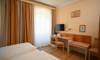 A bright and cozy room with two beds. The room is equipped with a desk and a television, as well as large windows that let in plenty of light.
