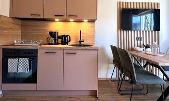 A modern kitchen with bright cabinets and appliances. Next to the kitchen, there is a dining area with elegant chairs and a table.