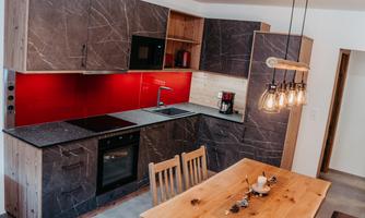 A modern kitchen with gray furniture and red back wall design. The wooden dining table complements the stylish interior.