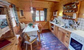 A cozy wooden kitchen with rustic charm. The table is lovingly set, surrounded by wooden chairs and practical kitchen shelves.