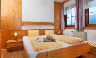 A cozy bedroom with a double bed and wooden paneling. The windows let in plenty of daylight and offer a view of the surroundings.