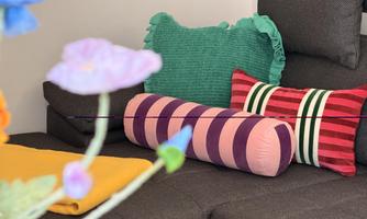 A cozy sofa with colorful cushions in various colors. In the foreground, some flowers are visible, adding a fresh touch to the picture.