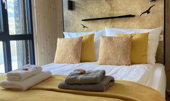 A cozy bedroom with a large bed and decorative pillows. The warm shades of yellow and the modern wall design create an inviting atmosphere.