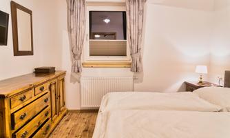 A cozy bedroom with two single beds and a wooden wardrobe. The room has bright walls and a window with curtains.