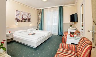 A cozily furnished room with a double bed and a modern television. The bright colors and floral pictures create a pleasant atmosphere.