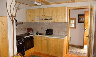 A bright kitchen with wooden cabinets and modern appliances. There is an open access to a hallway with a door and a window.