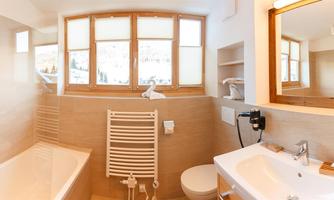 A modern bathroom with a bathtub and a sink. Large windows provide plenty of daylight and a view of the surroundings.