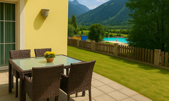 A sunny terrace with a table and chairs made of rattan. In the background, green meadows and mountains can be seen under a clear sky.