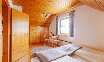 A cozy room with a wooden ceiling and two beds. There is a small dining area with a table and chairs.