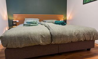 A cozy bedroom with two single beds and a modern wooden paneling. The bedding is in soft colors, and fresh towels are visible.