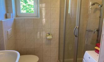 A bright bathroom with a shower, sink, and toilet. The walls are tiled, and a window provides natural light.