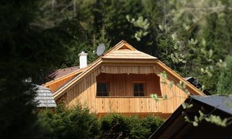 A cozy wooden house with a gabled roof, surrounded by trees. The windows are inviting and the architecture is rustic.