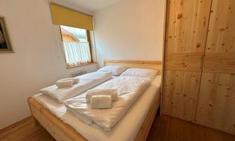 A cozy bedroom with a wooden double bed and fresh bedding. The bright walls and window create a friendly atmosphere.