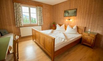 A cozy room with wooden walls and a double bed.  
Next to the bed is a nightstand, and the window offers a beautiful view.