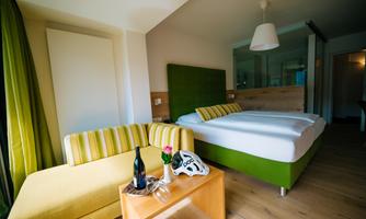 A modern bedroom with a large bed and a cozy sitting area. The color scheme in green and yellow creates an inviting atmosphere.