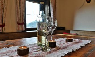 A bottle of wine is on a table, along with two wine glasses and a few candles. In the background, curtains and a window can be seen.