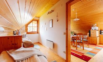 A cozy attic room with wooden walls and a window. The space is bright and inviting, with a dining area and a colorful rug.