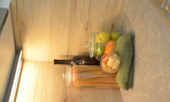 A cozy kitchen corner with glass containers holding pasta and apples. A bottle of wine and a green cloth complement the scene.