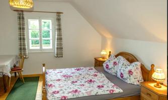A cozy bedroom with a large bed and floral bedding. The room has two windows and a simple, inviting decor.